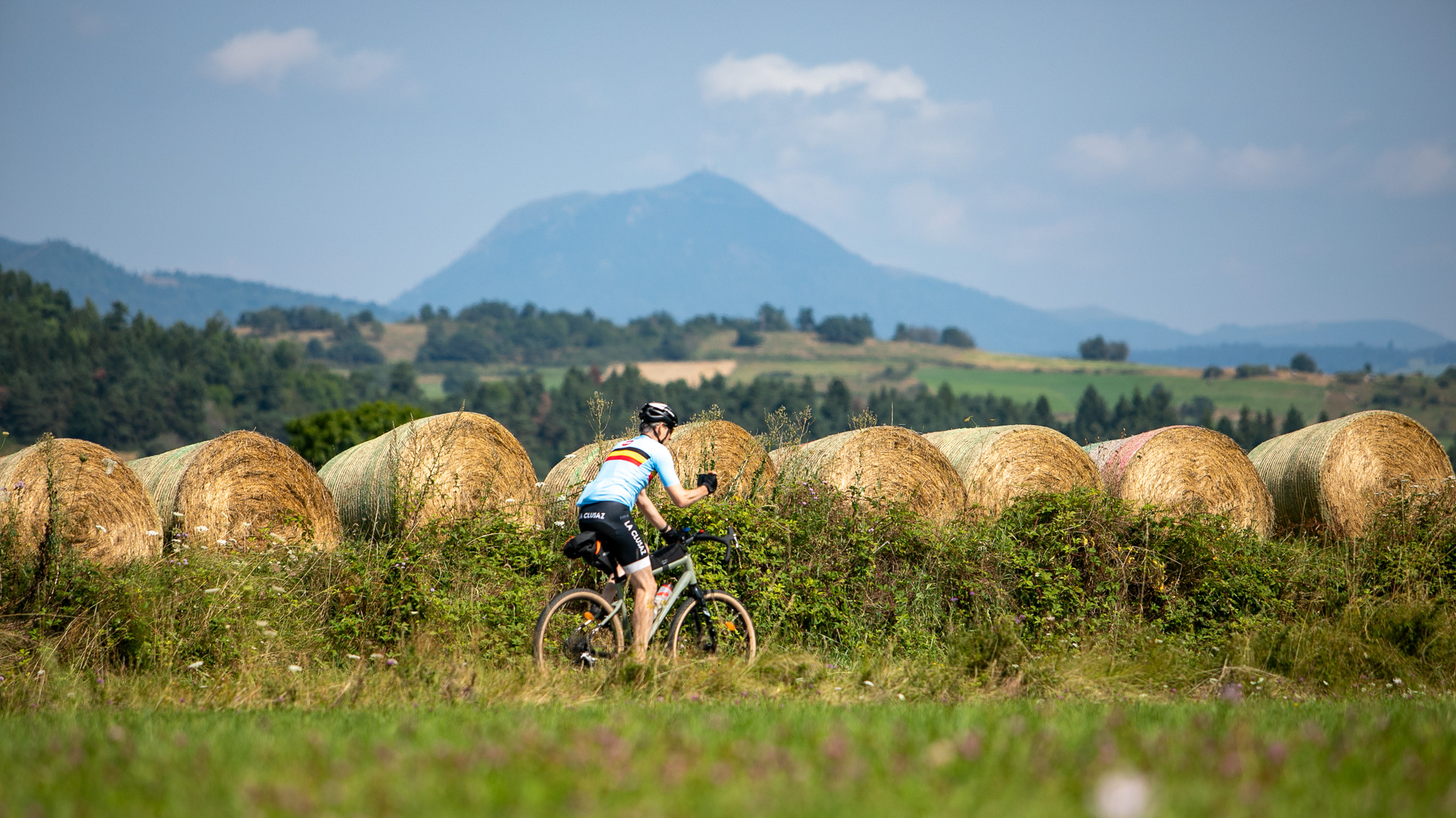 cycliste sur son vélo gravel dans les volcans d'Auvergne avec le puy de Dôme en fond