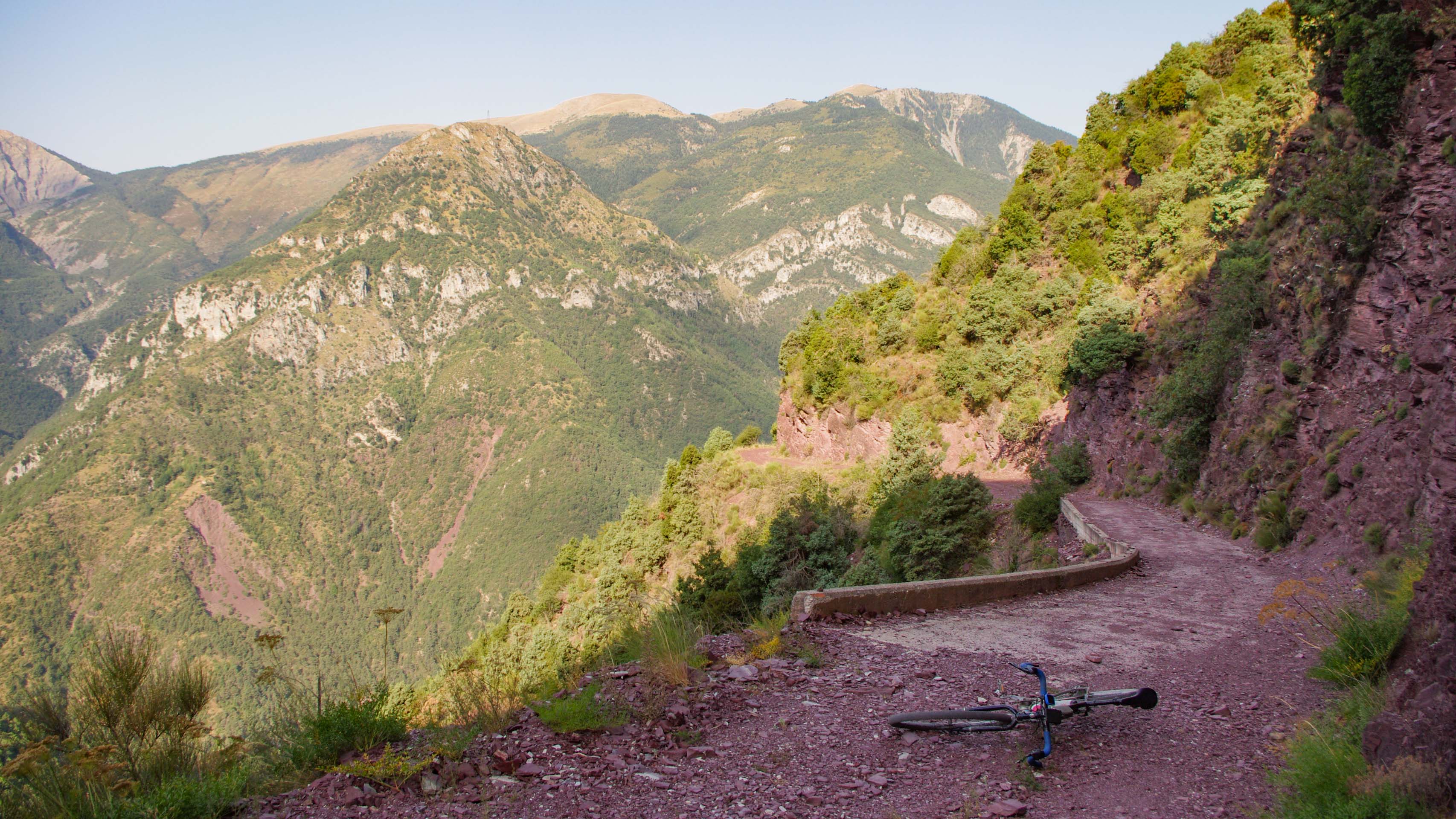 vélo posé sur une piste en balcon revêtue d'une terre rouge naturelle dans la vallée de la Tinée, en direction du col de Colmiane dans le Mercantour