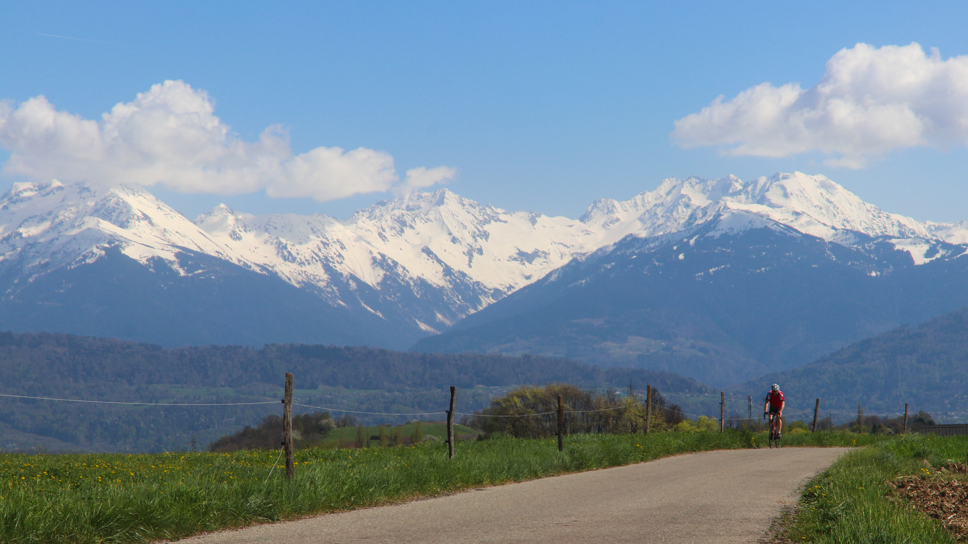 un cycliste parcours la route V63 avec la chaine de Belledonne en arrière-plan