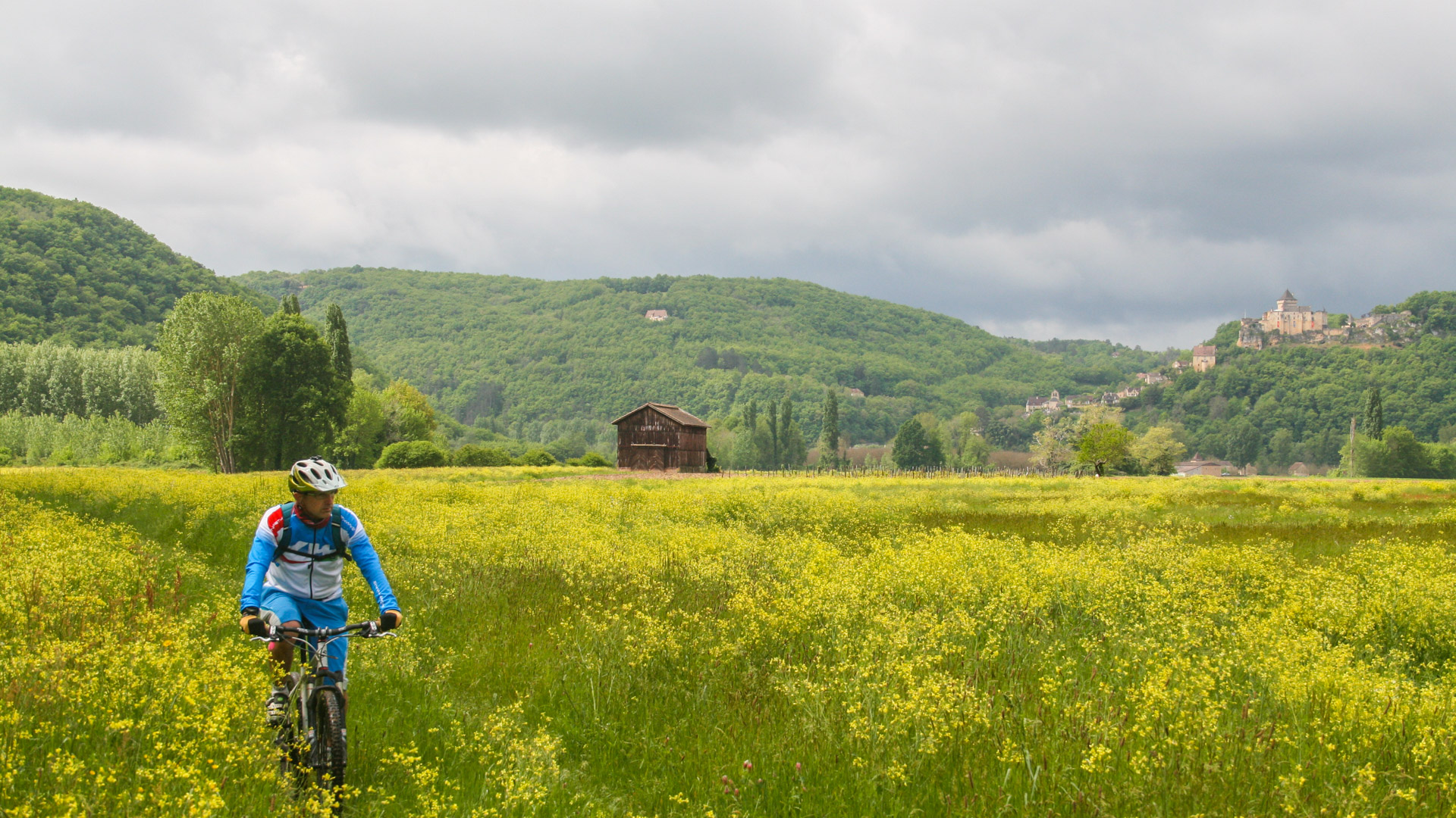 homme à VTT dans un champs fleuri avec en fond un château médiéval périgourdin