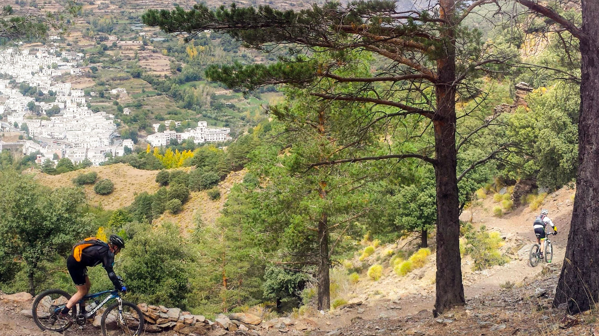 vttistes sur un single et en arrière plan un petit village blanc des alpujarras en espagne